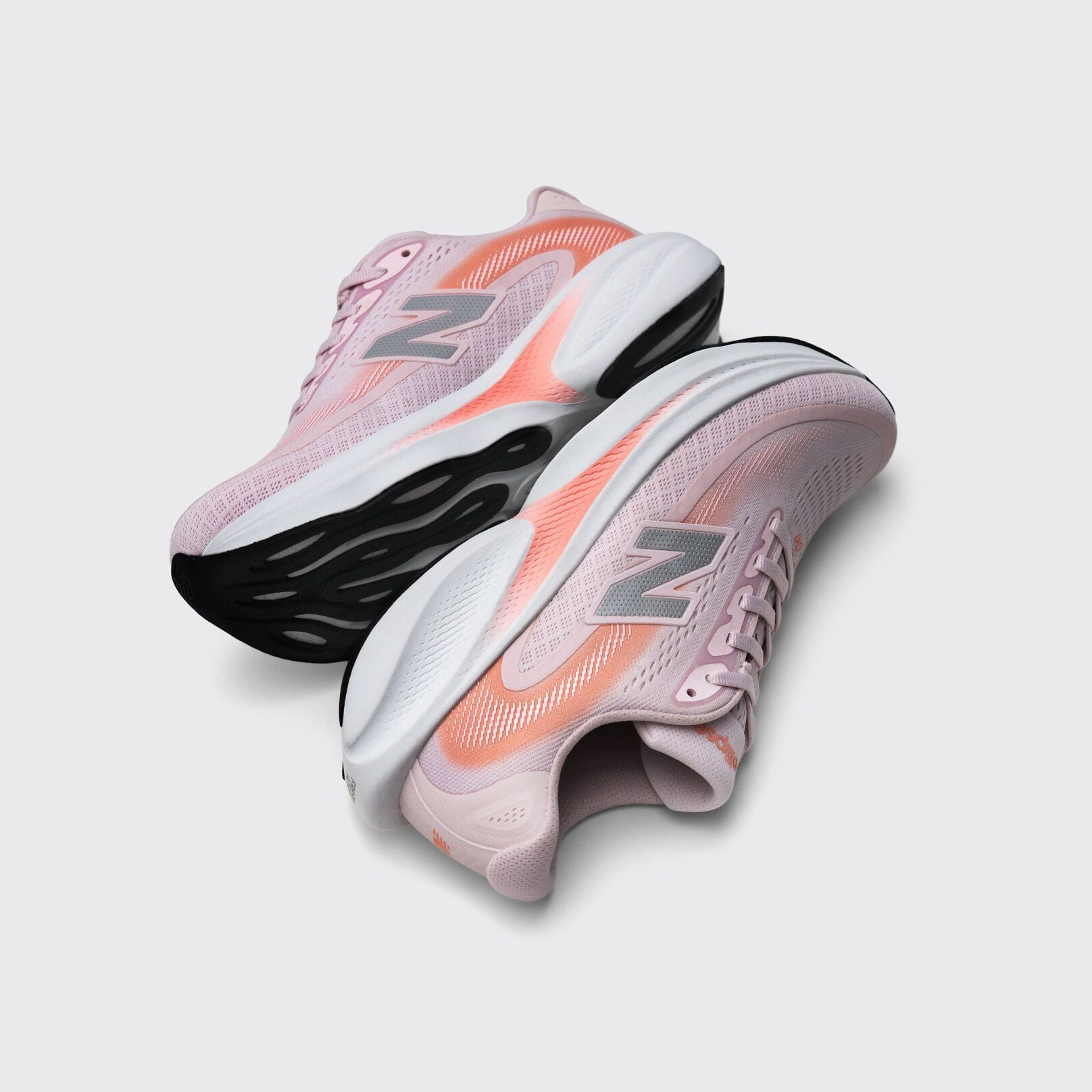 Pair of light pink New Balance running shoes with coral accents and chunky black-and-white soles displayed on a light gray background.